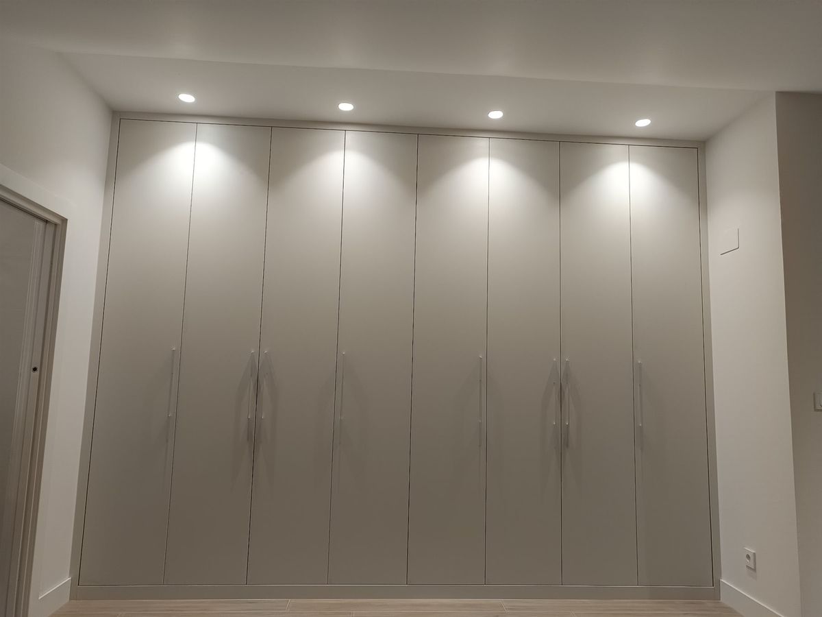Armario de frente completo. Puertas abatibles y frente de suelo a techo bajo iluminación puntual.