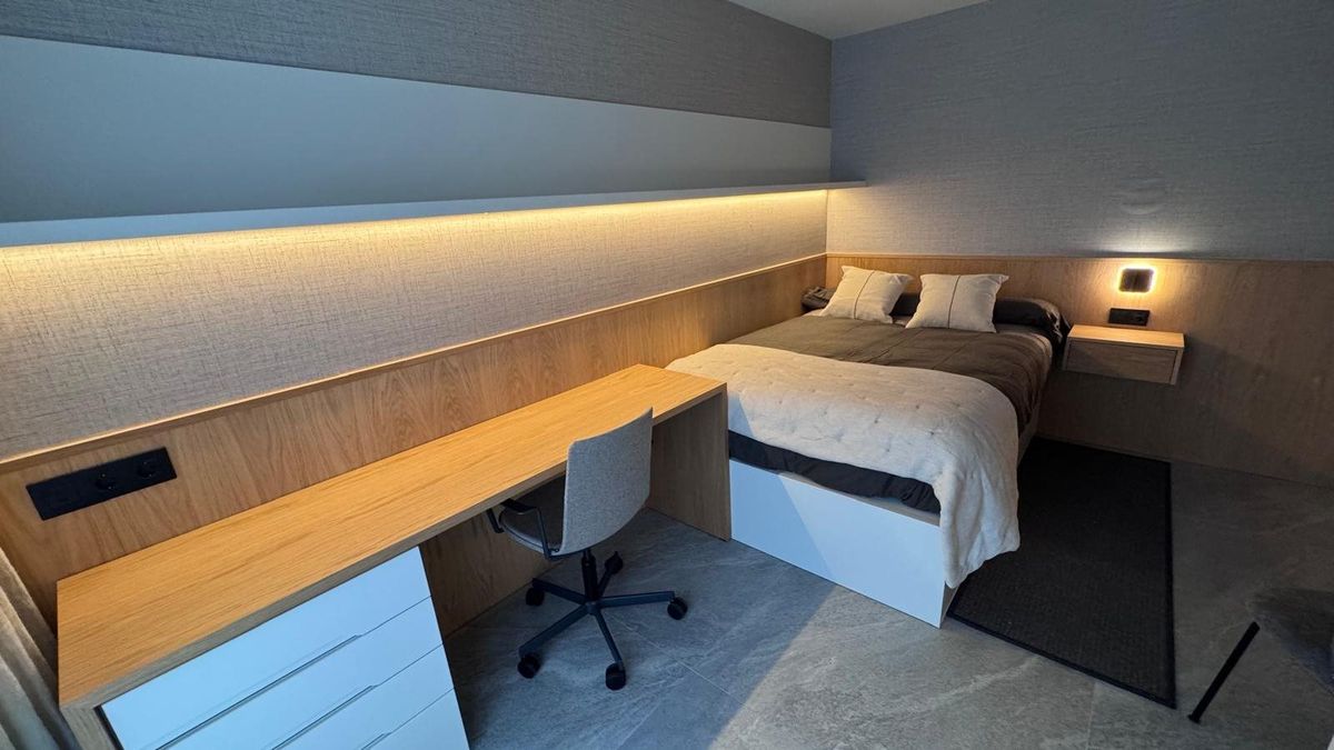 Dormitorio con escritorio integrado. Cabecero, mesilla y superficie de trabajo en un mismo conjunto.
